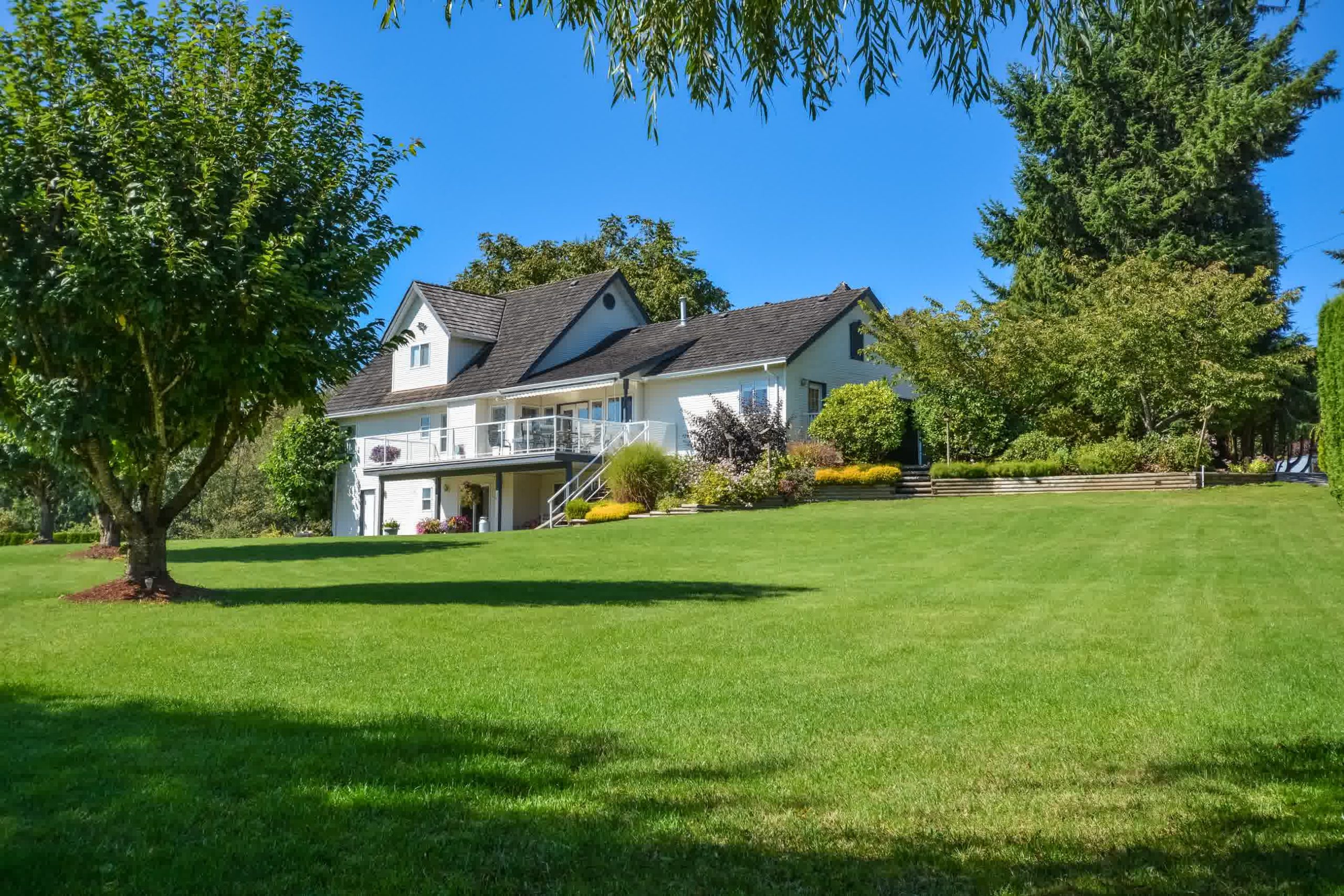 Large green weed-free lawn in front of a white two-story home, maintained with professional weed control and regular lawn treatments.